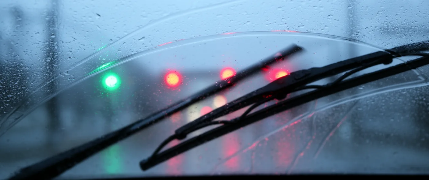A wiper blade mid-sweep across a wet windscreen, leaving a smeared streaky arc where it has cleared instead of wiped.
